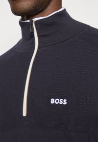 Sweatshirt azul marinho de meia abertura com um acabamento texturizado, apresentando um logótipo "BOSS" branco bordado e detalhes de fecho destacar.
