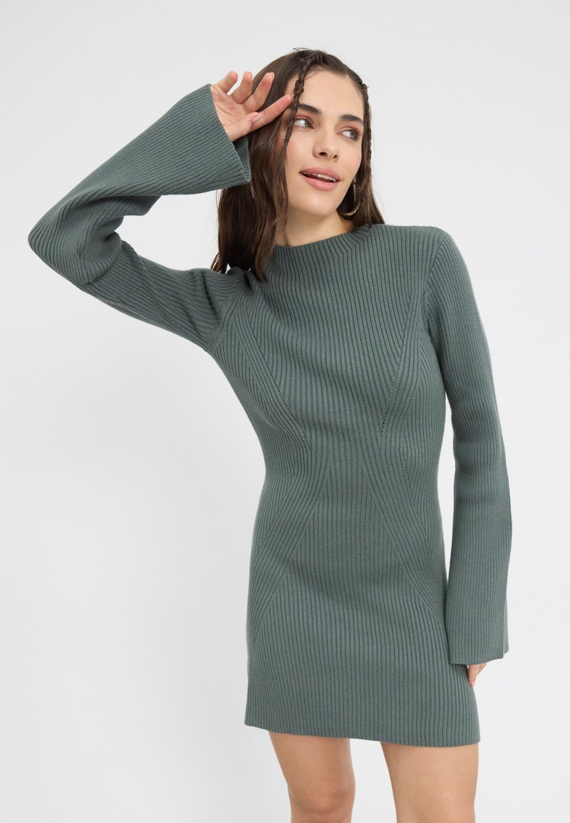 Abito a maniche lunghe a coste di un verde smorzato. Silhouette aderente con maniche ampie e dettagli di cucitura diagonale. Tessuto morbido, lunghezza fino al ginocchio.