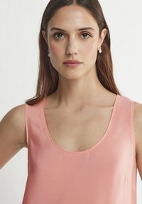 Ärmlös rosa topp med rundad halsringning, tillverkad av ett slätt tyg. Enkel design utan synliga mönster eller detaljer.