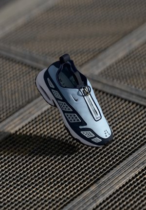 Nike sportbačiai turi beužsegamą dizainą, šviesiai mėlyną viršutinę dalį, juodus akcentus ir perforuotas šonines dalis. Apvalus pirštas ir tekstūruota pado dalis.