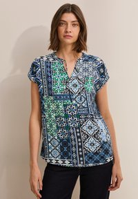 Top a maniche corte, blu con motivo floreale che presenta vari disegni in verde, blu scuro e bianco; scollo a V e vestibilità ampia.