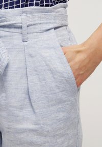 Ljusblå linnebyxor med en bred midja, veckad design och sidofickor. Tyget har en texturerad, subtil randig mönstring.