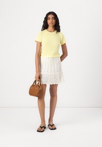 Camiseta amarilla de manga corta, falda blanca de encaje, bolso acolchado marrón, chanclas negras. Diseño sencillo, texturas suaves y patrones superpuestos.