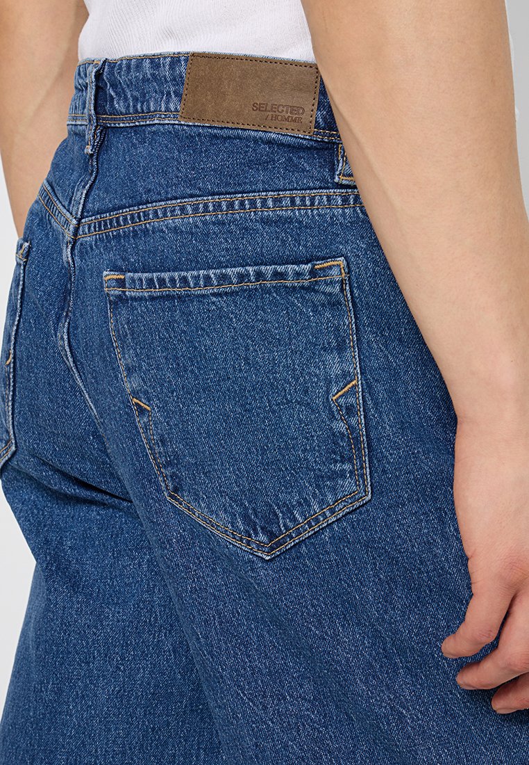 Donkerblauwe denim jeans met een rechte snit, voorzien van een bruin leren label op de tailleband en standaard achterzakken met gele stiksels.