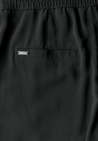 Černé tkaninové šortky s elastickým pasem a malou kovovou visačkou na zadní kapse. Hladká textura s minimálními detaily.