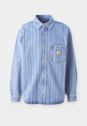 Camisa de denim azul claro con rayas verticales blancas, cuello tipo polo, cierre frontal abotonado, un bolsillo en el pecho y parche con el logo de Carhartt.