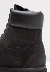 Czarne wodoodporne buty z gładką skórzaną cholewką, teksturowanym welurowym korpusem, okrągłymi sznurowsadłami, wyściełanym kołnierzem oraz wytłoczonym logo na pięcie.