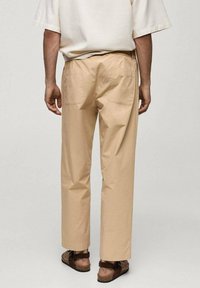 Bež, lahki bombažni hlače s ravnim krojem, dvema zadajnima žepoma in gladko teksturo, kombinirane s svetlo rjavimi sandali.
