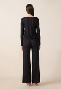 Μαύρη μπλούζα με μακριά μανίκια και χαλαρή εφαρμογή, συνδυασμένη με μαύρο παντελόνι με φαρδιά πόδια. Ελαφρύ, υφασμάτινο υλικό με χαλαρή γραμμή.