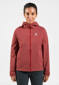 Red outdoor jacket with a hood, full-length zipper, and logo on the chest. Features zippered pockets and adjustable cuffs. Smooth texture.