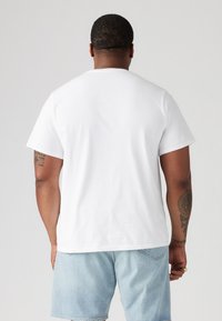 Witte katoenen t-shirt met een ronde hals en korte mouwen, gezien vanuit de achterkant. G gedragen met lichte denim shorts.