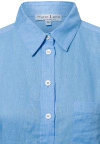 Camicia di lino azzurra chiara con colletto classico, chiusura a bottoni e una tasca sul petto. Presenta bottoni in plastica e una finitura testurizzata.