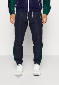 Námořnické tepláky s zelenými bočními panely, bílou stahovací šňůrkou a logem. Materiál má hladký povrch a elastické manžety na kotnících.