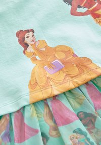 Tricou albastru deschis cu o grafică galbenă a unei prințese în partea superioară, stratificat cu o fustă transparentă cu ilustrații colorate ale prințeselor.