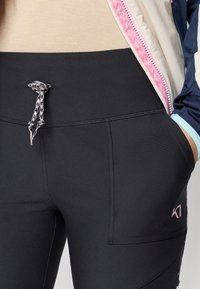 Svarte treningsbukser med elastisk linning, som har snøre, sidelommer og en subtil rosa logo på venstre side.