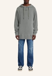 Grå huva med justerbara snören, två framfickor och en avslappnad passform, kombinerad med slitna blå jeans och svart-vita sneakers.