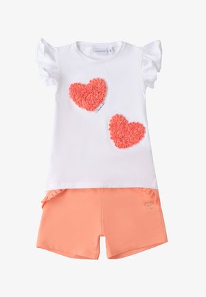 Weißes Baumwoll-T-Shirt mit Rüschensleeves, ausgestattet mit zwei strukturierten korallfarbenen Herzapplikationen, kombiniert mit korallfarbenen Shorts.