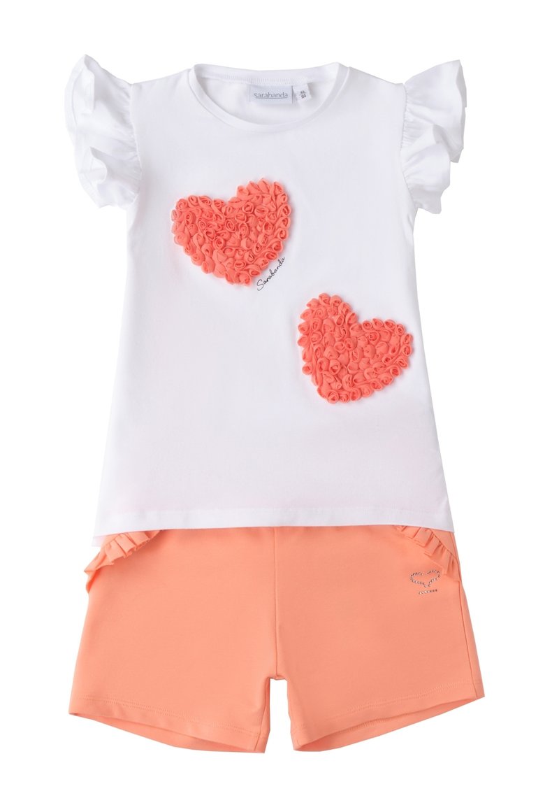 Camiseta blanca de algodón con mangas acampanadas, que presenta dos apliques de corazón en textura coral, combinada con pantalones cortos color coral.