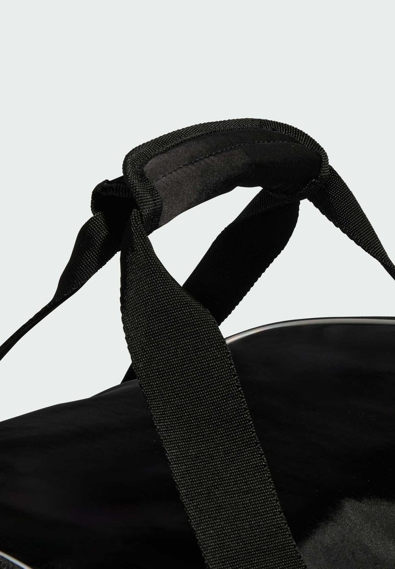 Schwarze Stofftasche mit breitem, gepolstertem Griff und stabilen gewebten Trägern vor hellem grauem Hintergrund.