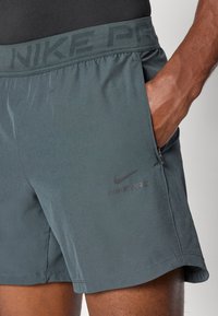 Tumši pelēki Nike Pro šorti ar teksturētu jostasvietu, sānu kabatu un diskrētu melnu logotipu. Viegls audums ar gludu apdari.
