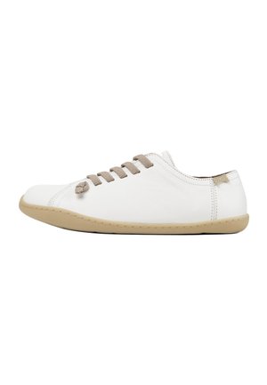Hvid lædersneaker med beige snørebånd og en lys tan gummisål. Har et minimalistisk design og synlige syninger langs siderne.