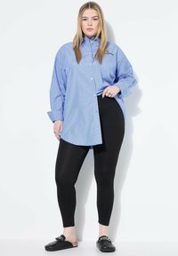 Sininen raidallinen paita, jossa on napitettava kaulus, ylipitkä malli, yhdistettynä mustiin legginsseihin ja mustiin liukuhihnakenkiin, joissa on ketjuseos.