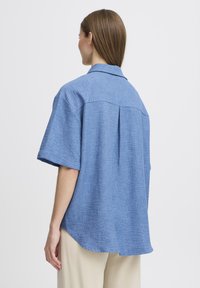Camicia azzurro chiaro a maniche corte con colletto, caratterizzata da una piega sul retro e una vestibilità comoda. Realizzata in un tessuto intrecciato testurizzato.