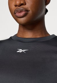 Čierny športový dres s okrúhlym výstrihom a jemnou textúrou. Na hrudi sa nachádza biele logo Reebok.