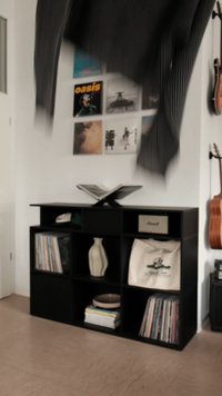 Estante de madeira preta com múltiplos compartimentos quadrados, apresentando um vaso decorativo, livros e uma bolsa. O fundo inclui discos de vinil.