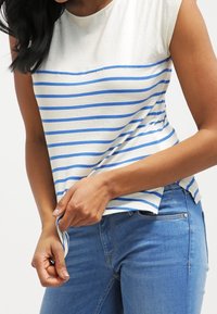 Camiseta de algodón a rayas con rayas horizontales azules y blancas, escote redondeado y mangas cortas, combinada con jeans azules.