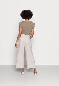 Oliwkowa bluzka na krótki rękaw w połączeniu z jasnobeżowymi spodniami o szerokich nogawkach. Spodnie mają kieszenie z tyłu i wysoki stan, a ich materiał jest gładki.