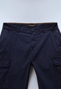 Marineblauwe cargobroek met knoop aan de voorkant, zijzakken en riemlussen, plat neergelegd op een lichte achtergrond.