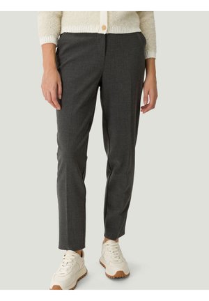 Femme portant un pantalon slim gris foncé, des baskets blanches et un cardigan crème avec un bouton en bois.