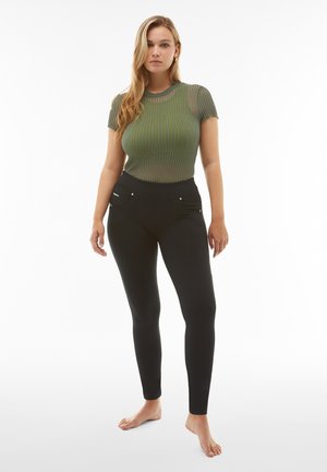 Grün gestreiftes Strickoberteil mit kurzen Ärmeln, kombiniert mit schwarzen, eng anliegenden Leggings mit Reißverschlusstaschen und glatter Stoffstruktur.