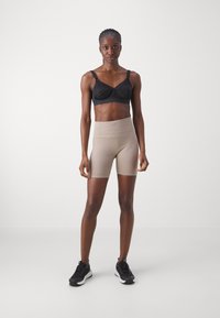 Svart bh med lett polstring, kombinert med beige ribbede høytaljede shorts. Modellen bruker svarte joggesko; jevn bakgrunn.