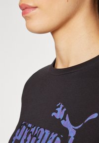 Svart bomull T-skjorte med lilla camouflasjemønster og logo på forsiden, rund hals og korte ermer.