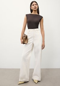 Brown fitted top, cream wide-leg jeans, and yellow pointed-toe shoes. Small brown handbag with structured design. Smooth textures and clean lines.