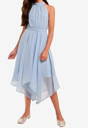 Robe sans manches bleu pâle à col licou, taille froncée et ourlet asymétrique à couches, portée avec des ballerines métalliques.