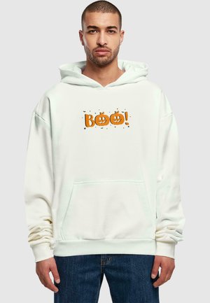Hvid hættetrøje med en orange "BOO!" grafik og græskar-motiver, en frontlomme og ribbede manchetter, parret med mørkeblå jeans.