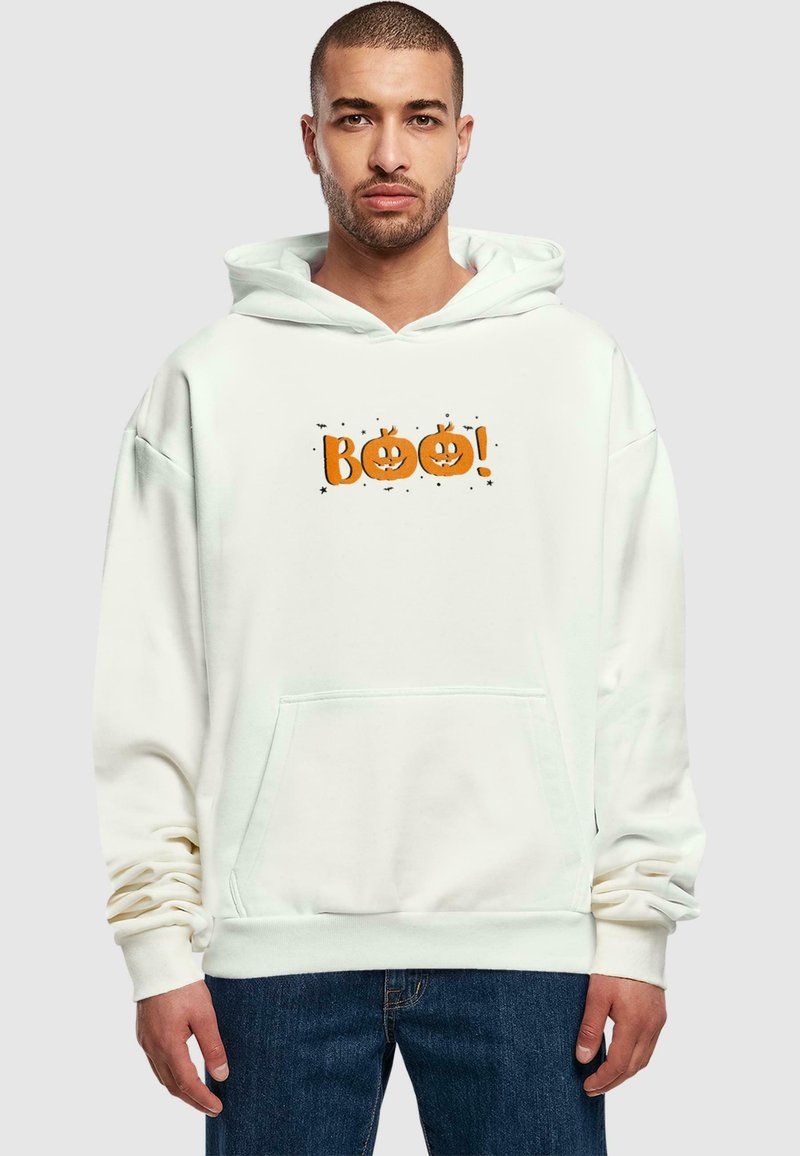 Hvid hættetrøje med en orange "BOO!" grafik og græskar-motiver, en frontlomme og ribbede manchetter, parret med mørkeblå jeans.