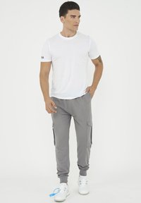 Vit t-shirt med rund halsringning och korta ärmar, kombinerad med grå smal tapered joggers med sidofickor och elastiska muddar. Bärs med vita sneakers.