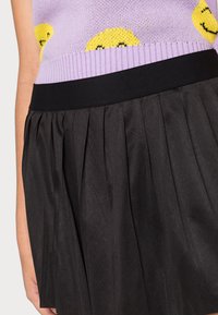 Top malha roxo com padrões de sorrisos, combinado com uma saia preta plissada com uma cintura lisa e tecido texturizado.