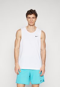 Bjeli majica bez rukava s okruglim izrezom i malim crnim Nike logotipom na prsima, u kombinaciji s svijetloplavi kratkim hlačama.
