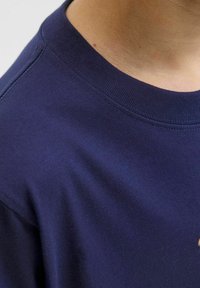 Námornícka modrá bavlnená tričko s ribovaným okrúhlym výstrihom. Mäkka textúra s jemným leskom; viditeľné švy a časť grafického dizajnu na prednej strane.