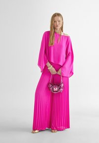 Top fucsia sin hombros con mangas anchas, combinado con una falda fucsia con pliegues. Los accesorios incluyen un bolso de lentejuelas con un logo de "M".