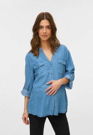 Denim srajca v svetlo modri barvi, z V-izrezom, dvema žepoma na prsih in gumbom na sprednji strani. Dolgi rokavi so zavihani do dolžine treh četrtin.