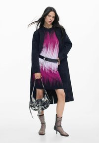 Fekete kabát rózsaszín-fehér, függőleges csíkos ruhán, texturált fekete övvel és mintás táskával párosítva. Az összhangot hálós bokacsizmák teszik teljessé.