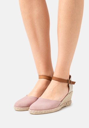Espadrilles compensées en suède rose avec une semelle en jute tressé beige et une bride de cheville marron. Design à bout rond avec une texture lisse et peu de détails.
