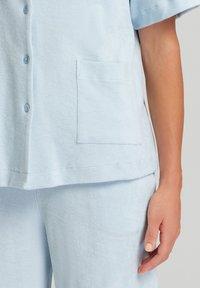 Completo da loungewear azzurro chiaro realizzato in tessuto testurizzato. Include una camicia con bottoni e taschino e pantaloni abbinati.