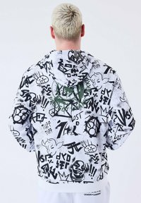Sudadera con capucha en blanco con estampados en estilo graffiti negro y acentos verdes, cuenta con cordón ajustable y puños acanalados.